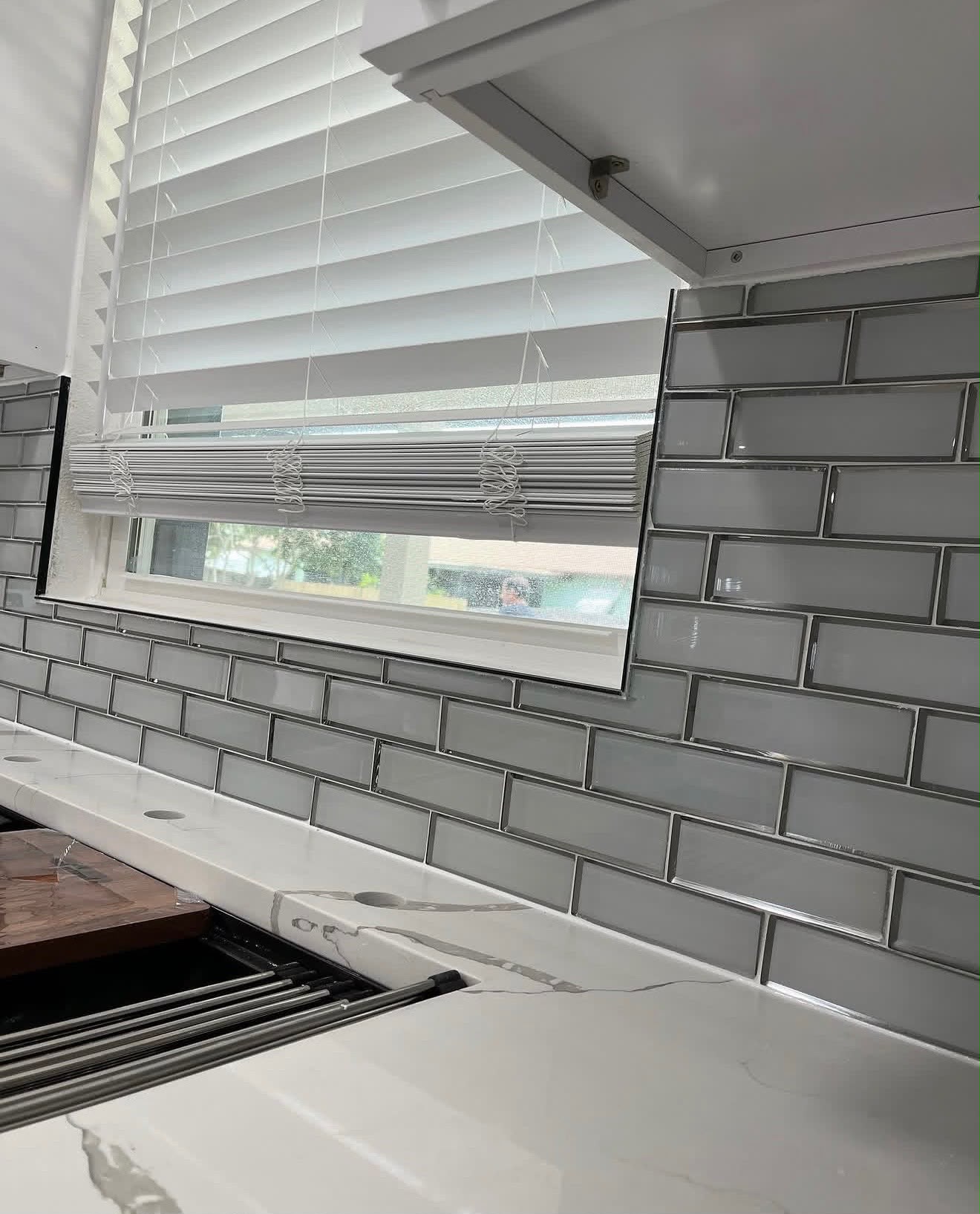 Glass subway tile backsplash being grouted around a window