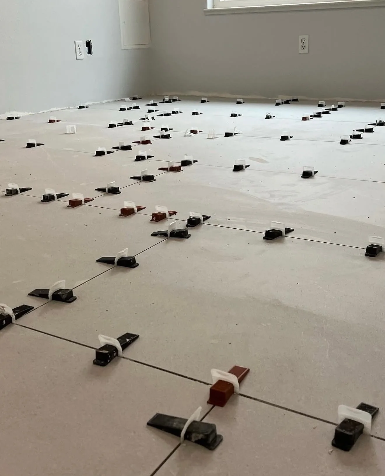 Close-up of leveling clips and spacers between large-format tile in a bedroom