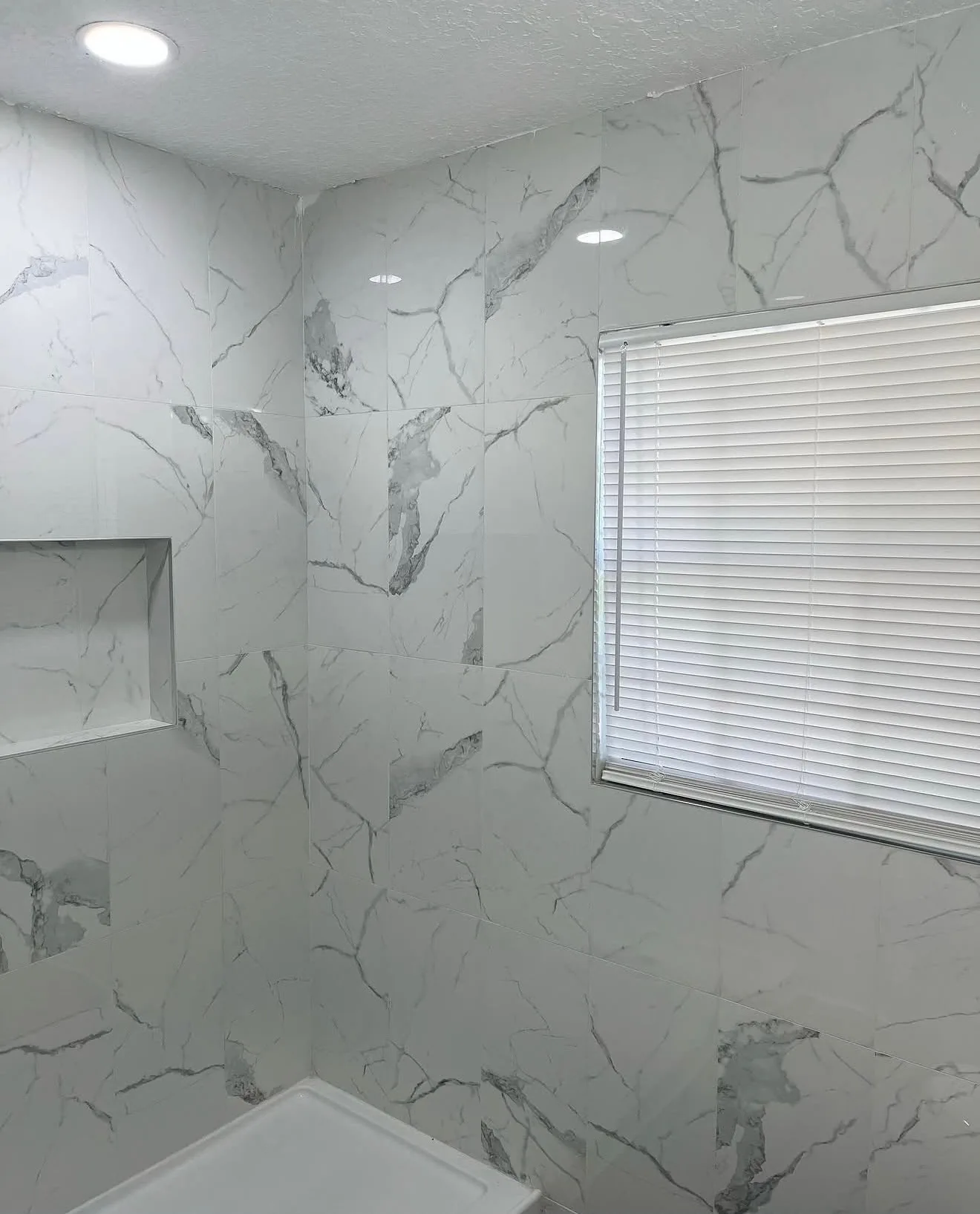Tub and shower wall in white marble-look tile with a recessed niche