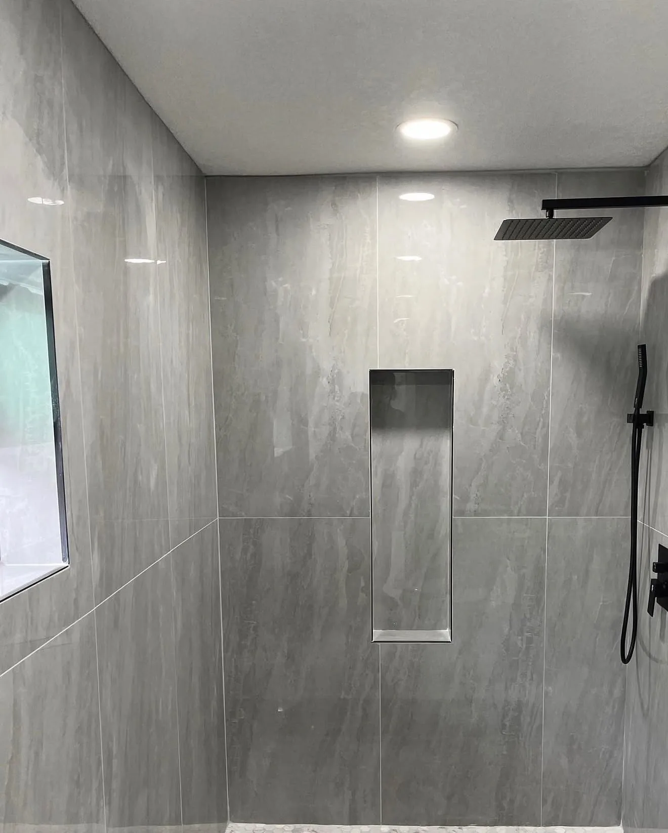 Corner of gray stone-look shower with matte black rain head and handheld wand