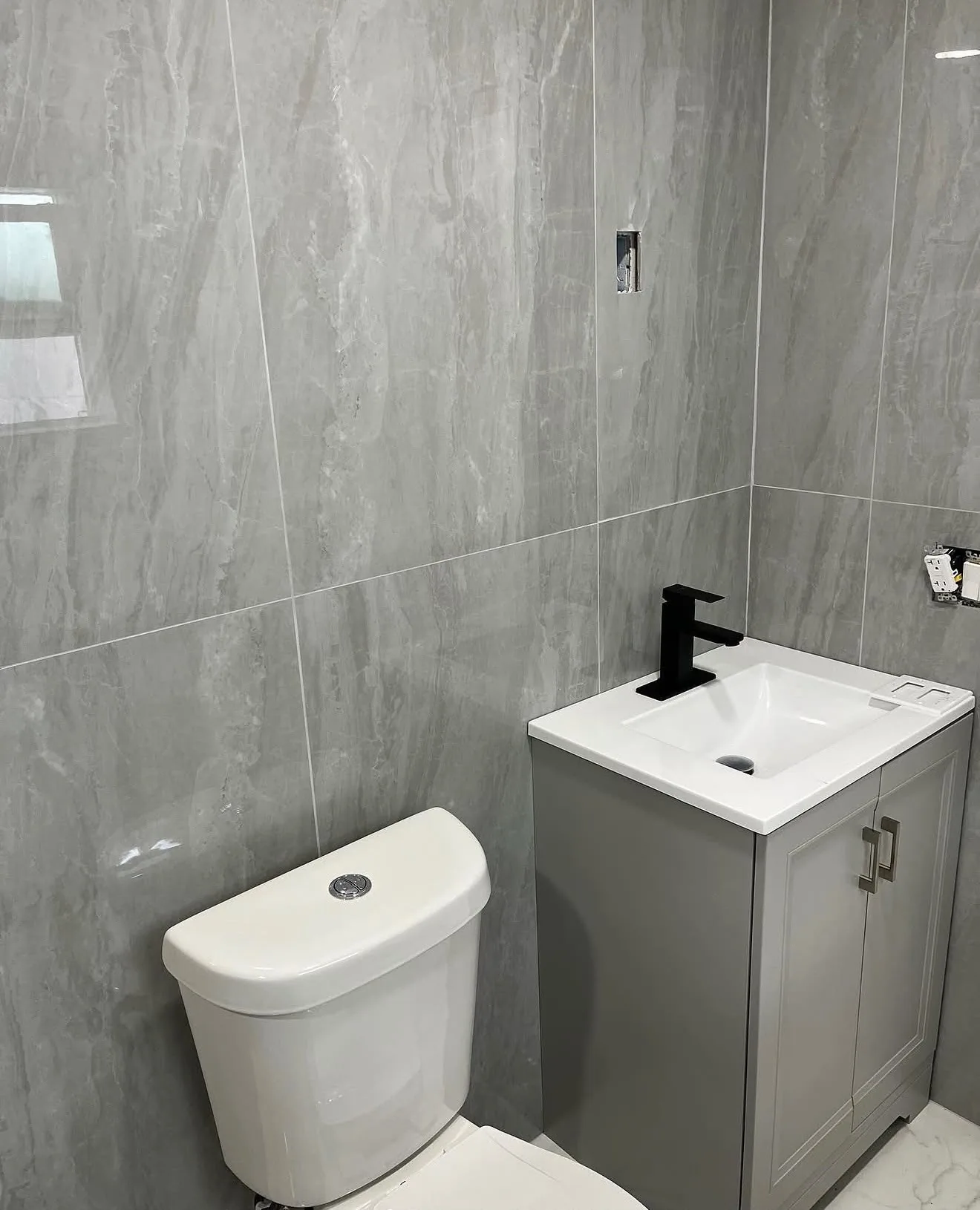 Gray stone-look tile vanity area with black faucet and toilet
