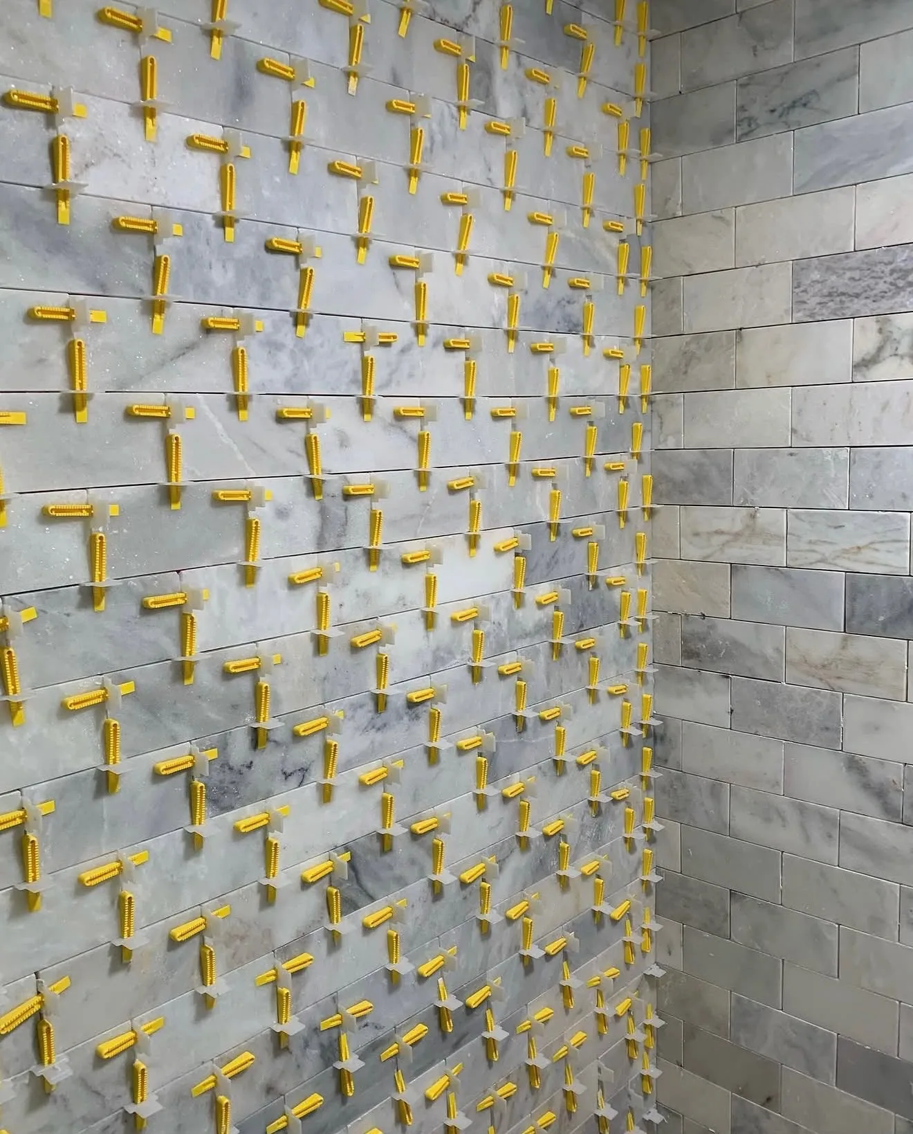 Full shower wall in marble subway tile with leveling clips still in place