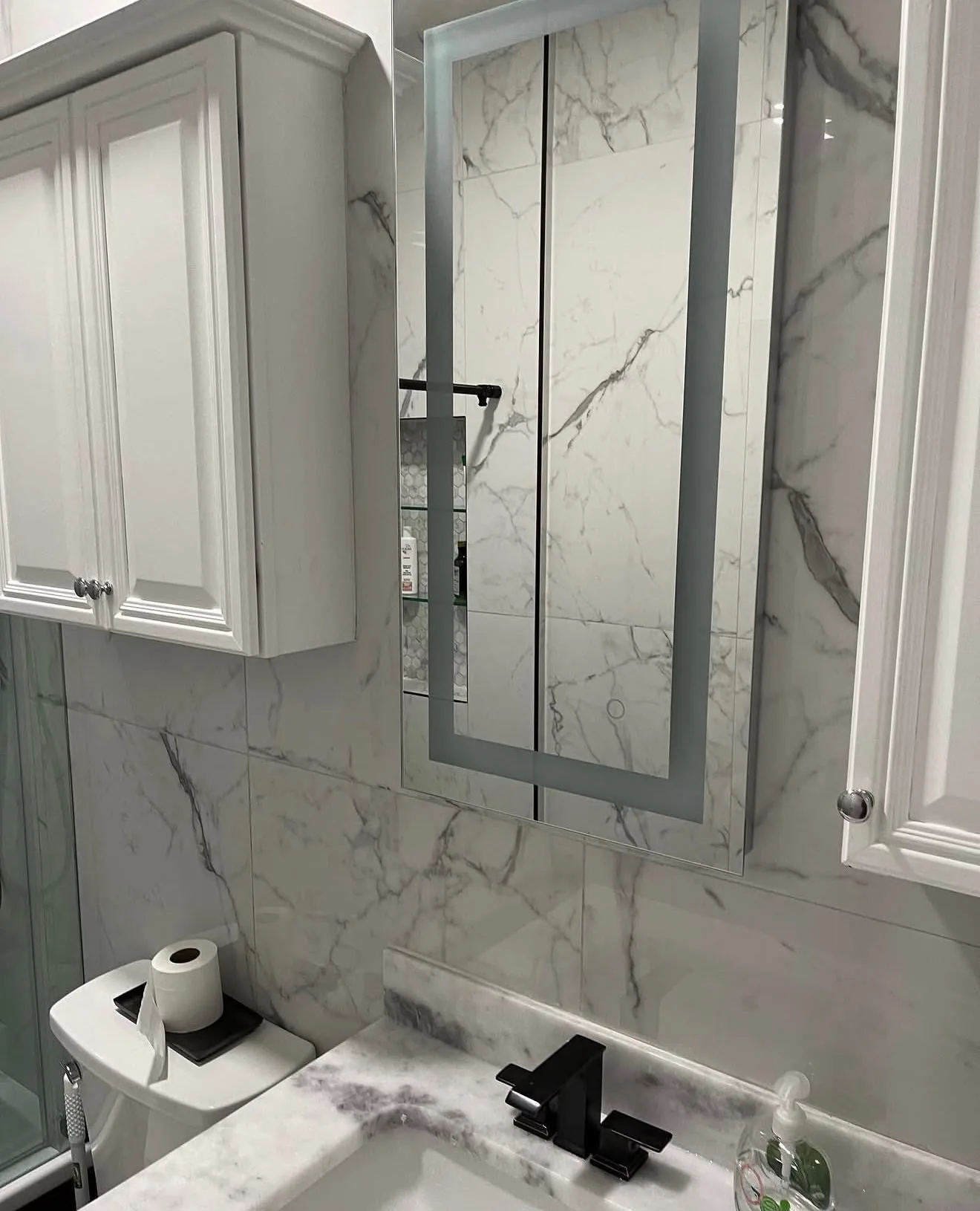 Marble-look tile wall and lit mirror above the vanity, reflecting the shower niche