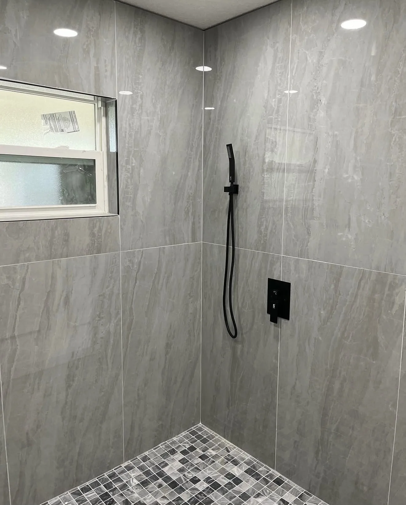 Corner of walk-in shower with matte black hand shower and valve
