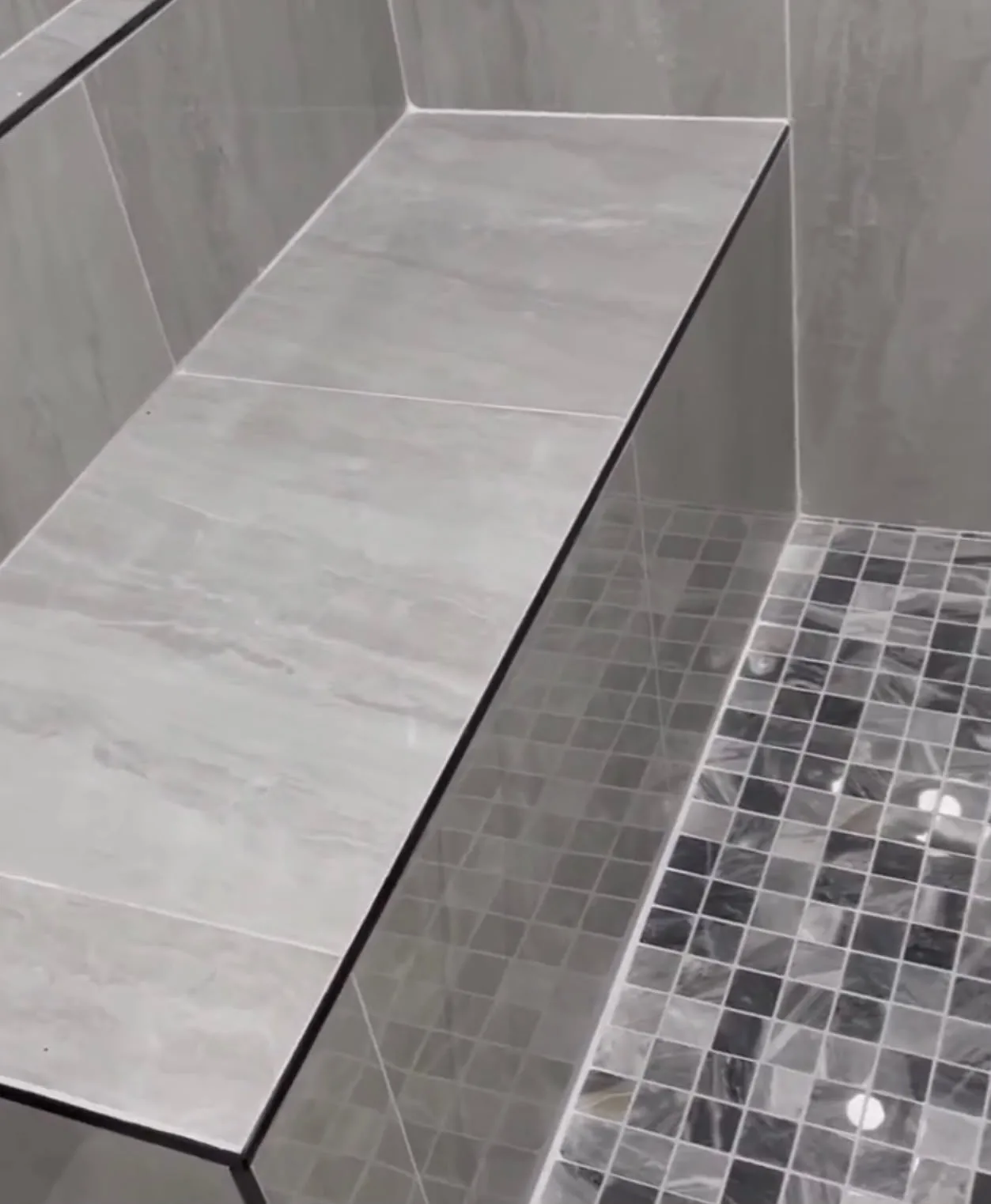 Close-up of tiled built-in shower bench with mosaic floor edge