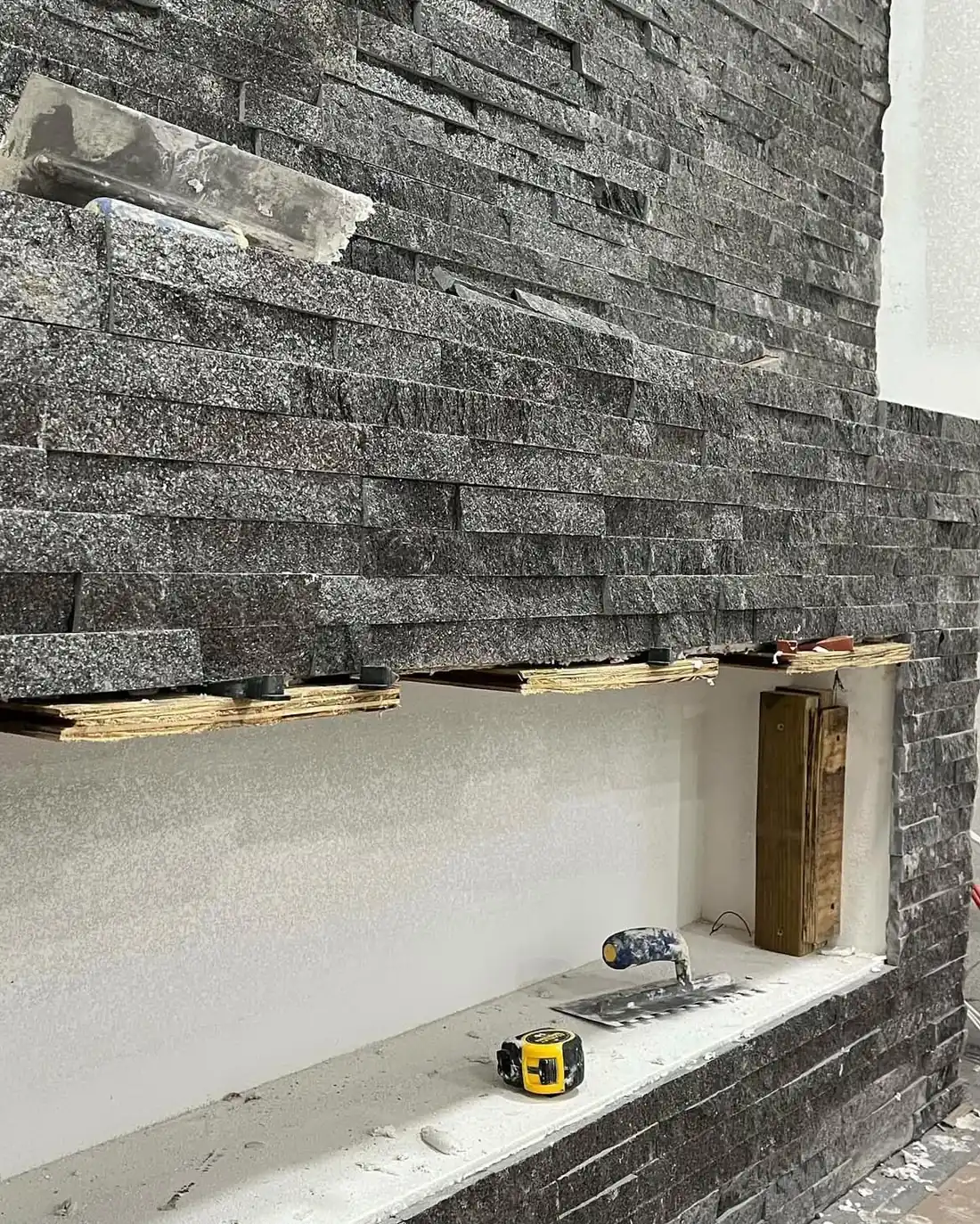 Split-face stacked stone veneer being installed on the fireplace wall