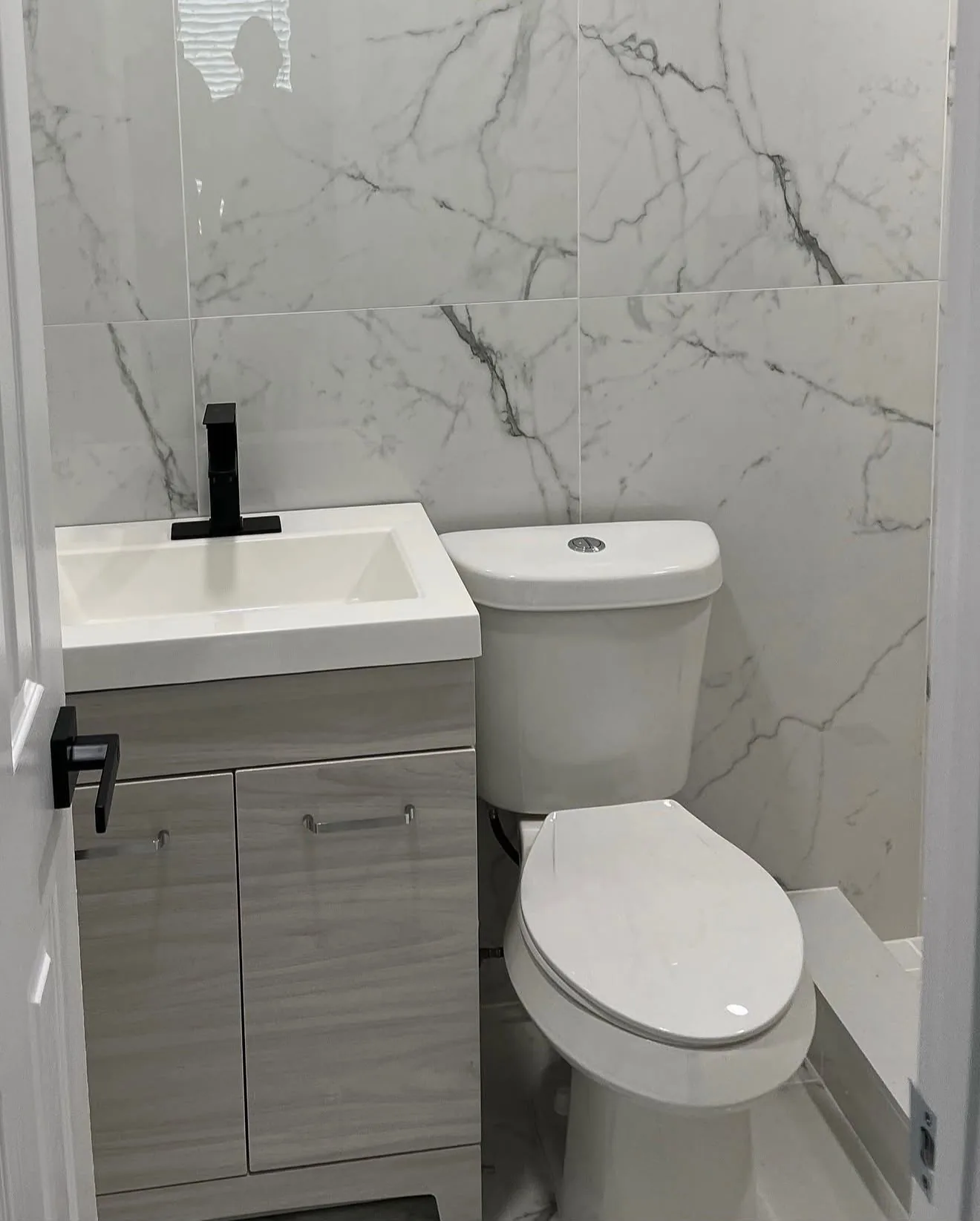 Full bathroom view with white marble-look tile, vanity and toilet